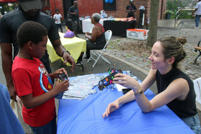 A Brooklyn Library staff engages a youngster with a paper toy train at the 16th Annual Back-to-School Harvest Fest hosted by Sen.Kevin Parker at Paerdegat Park, in the 21st Senate District, Brooklyn on Aug. 26, 2023.