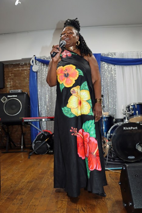 VINCI PRO and event coordinator Fern Dopwell addresses patrons, wearing a dress designed by late Vincentian mas producer Julian "Peling" Pollard. A moment of silence was observed at the event in honor of Pollard's recent passing.