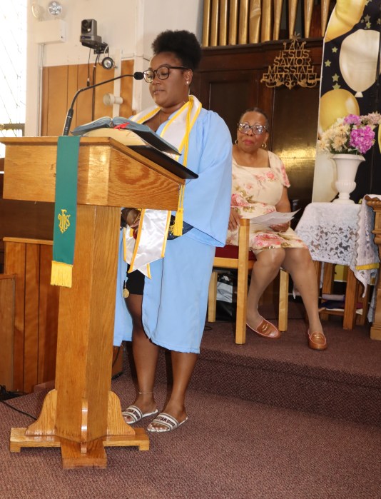 Zuria Thorpe addresses graduates, with Liturgist Min. Cynthia Grant seated in background.