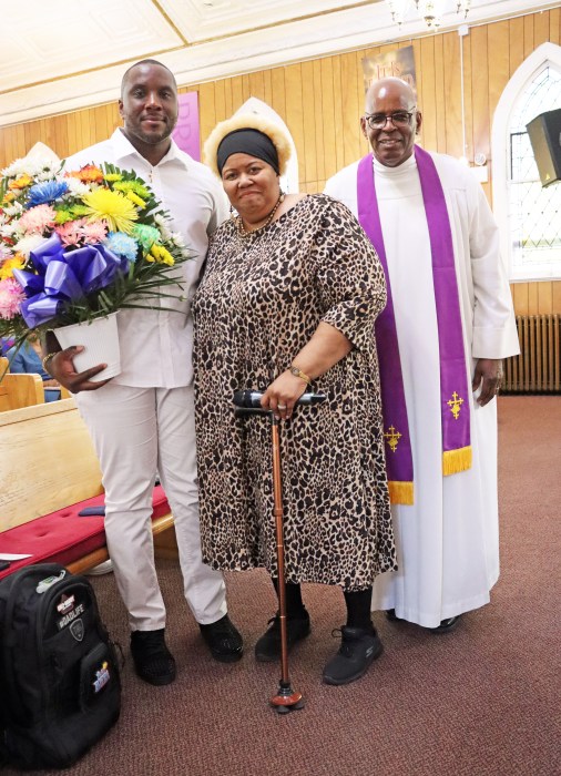 Sheldon Carty, 36, the youngest father in the congregation, receives a bouquet of flowers from Sis. Benita Lynn Malloy, president of the United Women of Faith at Fenimore Street United Methodist Church, and Pastor, the Rev. Roger Jackson, (right).