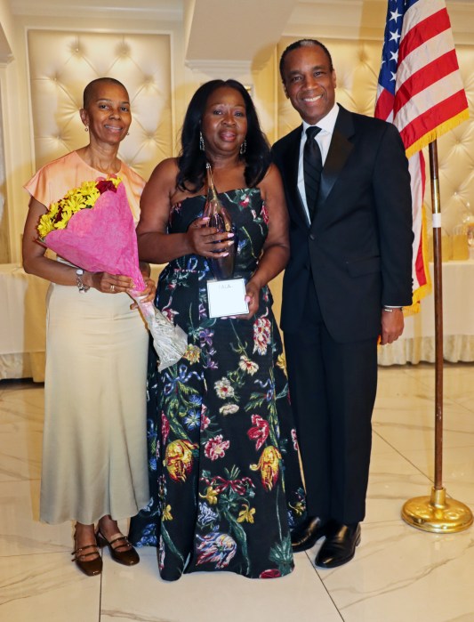 Justice Sylvia Hinds-Radix holds award, flanked by Justice Ruth Shillingford, holding bouquet of flowers, and Rudyard Whyte.
