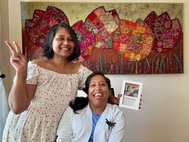 Lakshmee Lacchman-Persad (left) and her sister Annie Lachhman in front of a colorful painting.