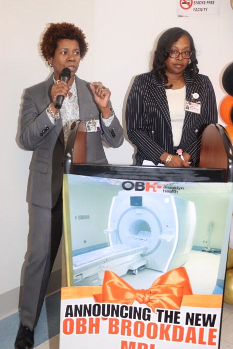 Dr. Sandra Scott, interim CEO of OBH, addresses the ribbon-cutting ceremony, flanked by Guyanese-American Sharon Devonish-Leid, OBH director of external/public affairs.