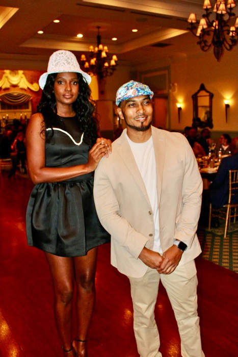 Model Stacey Godchild and Tony Hylton display hats donated by Grenadian fashion designer Fe Noel for the silent auction.