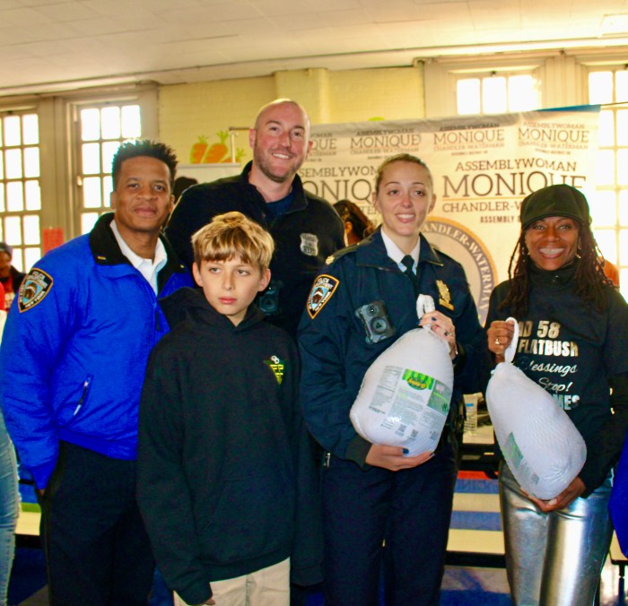 NYPD Deputy Inspector Kosak, PO Walsh, Lt McLean, and Caleb Kosk join Assembly Member Monique Chandler Waterman, far right, to distribute turkeys, sponsored by the politician, Busta Rhymes, Special Ed, LinkNYC, NYC Public Schools Chancellor Melisa Ramos and IAMWONDAWOMAN. From left are Celeste Terry, Superintendent District 18, Assembly Member Monique Chandler, Special Ed, handing over a turkey to a resident at the Annual Harvesting Health & Harmony Thanksgiving event at PS 135, on Linden Boulevard, Brooklyn.