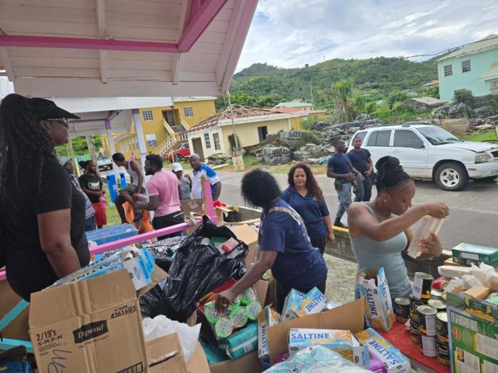 Assemblywoman Jaime Williams facing camera and her traveling disaster relief delegation dispensing supplies to the residents of Petit Martinique.