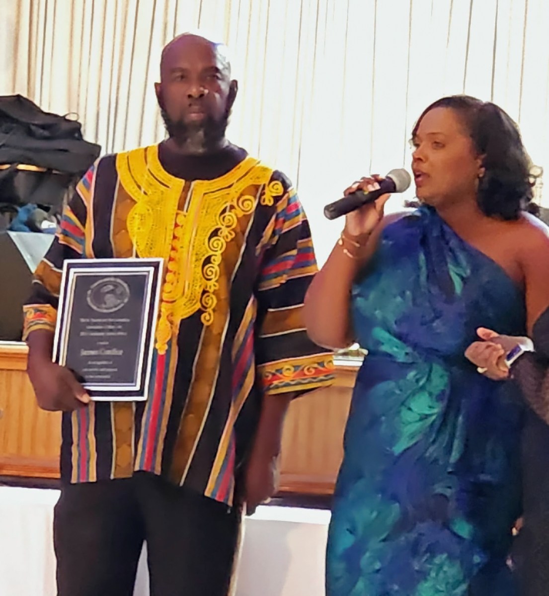 Jenell James, president of the St. Vincent and the Grenadines Association of Massachusetts, Inc., presents an award to James Cordice, a pioneer and coordinator of the St. Vincent and the Grenadines and Belize Penn Relays.