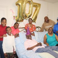 Mitchinson "Mitchie" James's flanked by daughters Hazel Morris, right, sitting on bed, and Angella Taylor, fourth from left (back), along with niece Daphne James, third from left, and other family members