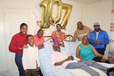 Mitchinson "Mitchie" James's flanked by daughters Hazel Morris, right, sitting on bed, and Angella Taylor, fourth from left (back), along with niece Daphne James, third from left, and other family members